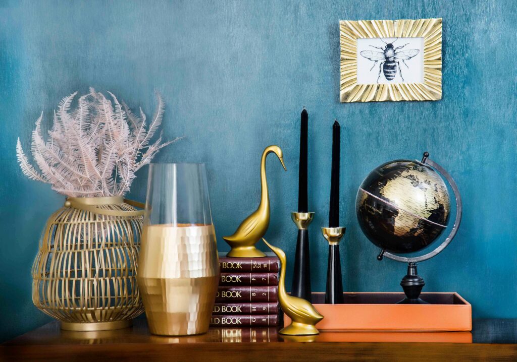 Stylish home decor arrangement including a globe, books, candles, and vases on a blue backdrop.