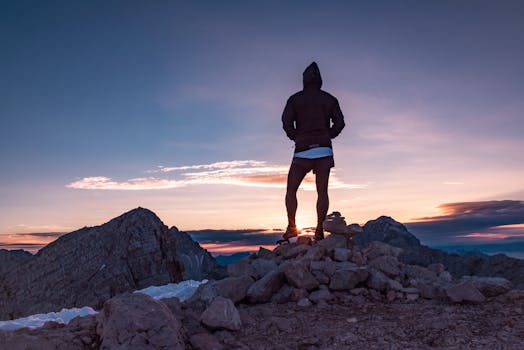 Person standing on a rocky mountain peak at sunset in Tolmin, Slovenia, embracing nature's beauty.